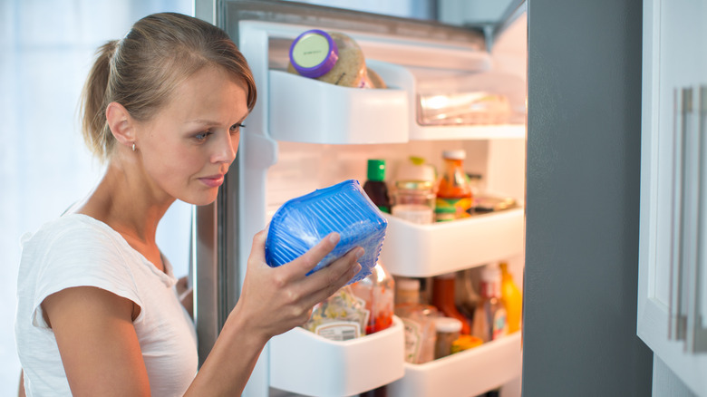 белая женщина проверяет этикетку на контейнере с продуктами из открытого холодильника