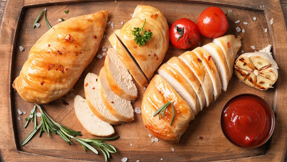 Приготовленная куриная грудка с розмарином и помидорами на разделочной доске