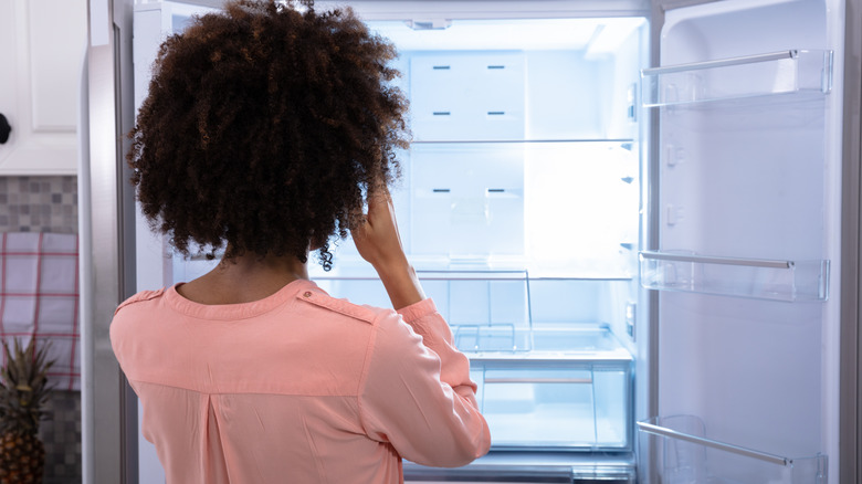 Женщина смотрит в пустой холодильник