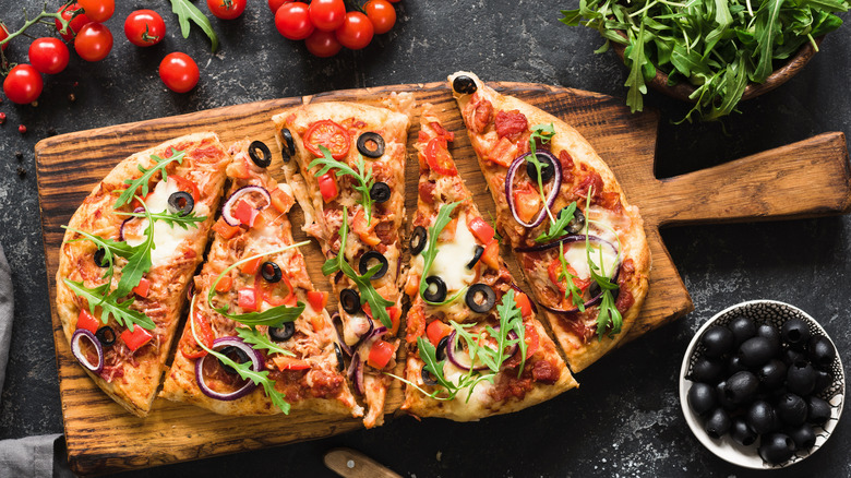 Вид сверху на овощную пиццу на деревянной доске рядом с оливками