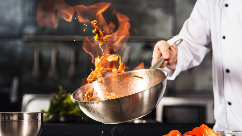 Шеф-повар подбрасывает горящие продукты в вок 