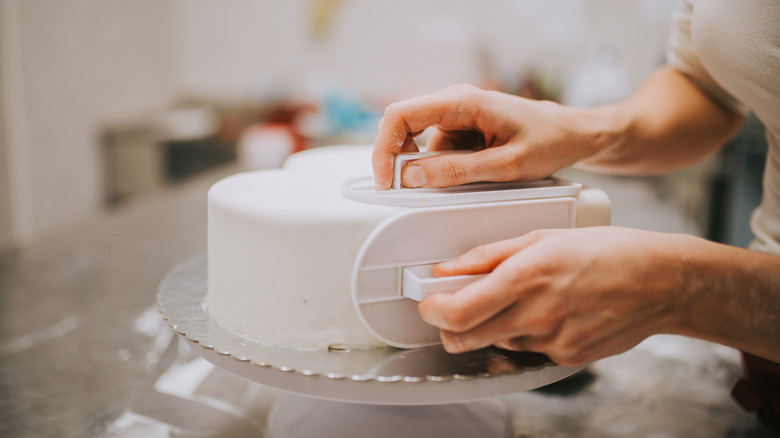 пекарь заворачивает торт в помадку